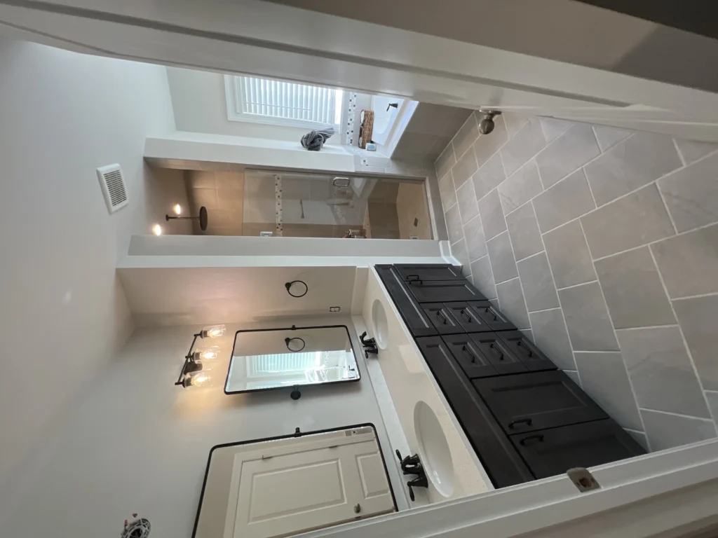 Modern bathroom with dual sinks, large mirror, and glass shower.